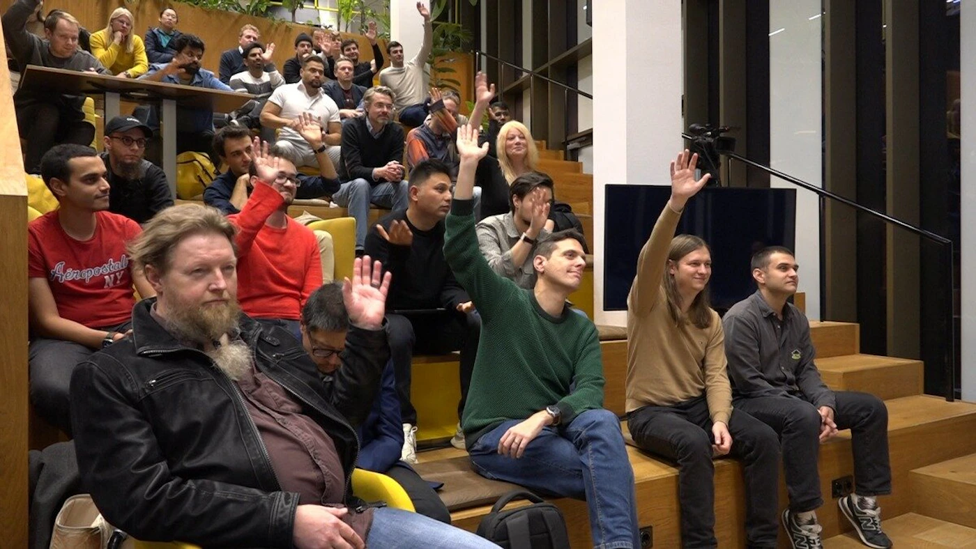 (Photo) A group of people are sitting in a tiered seating area, many with their hands raised. Text: Unprecedented NY people | indoor | group of people, raised hands, tiered seating, presentation setting | candid Note: The image is a real-life captured moment of a group of people, making it a photograph.