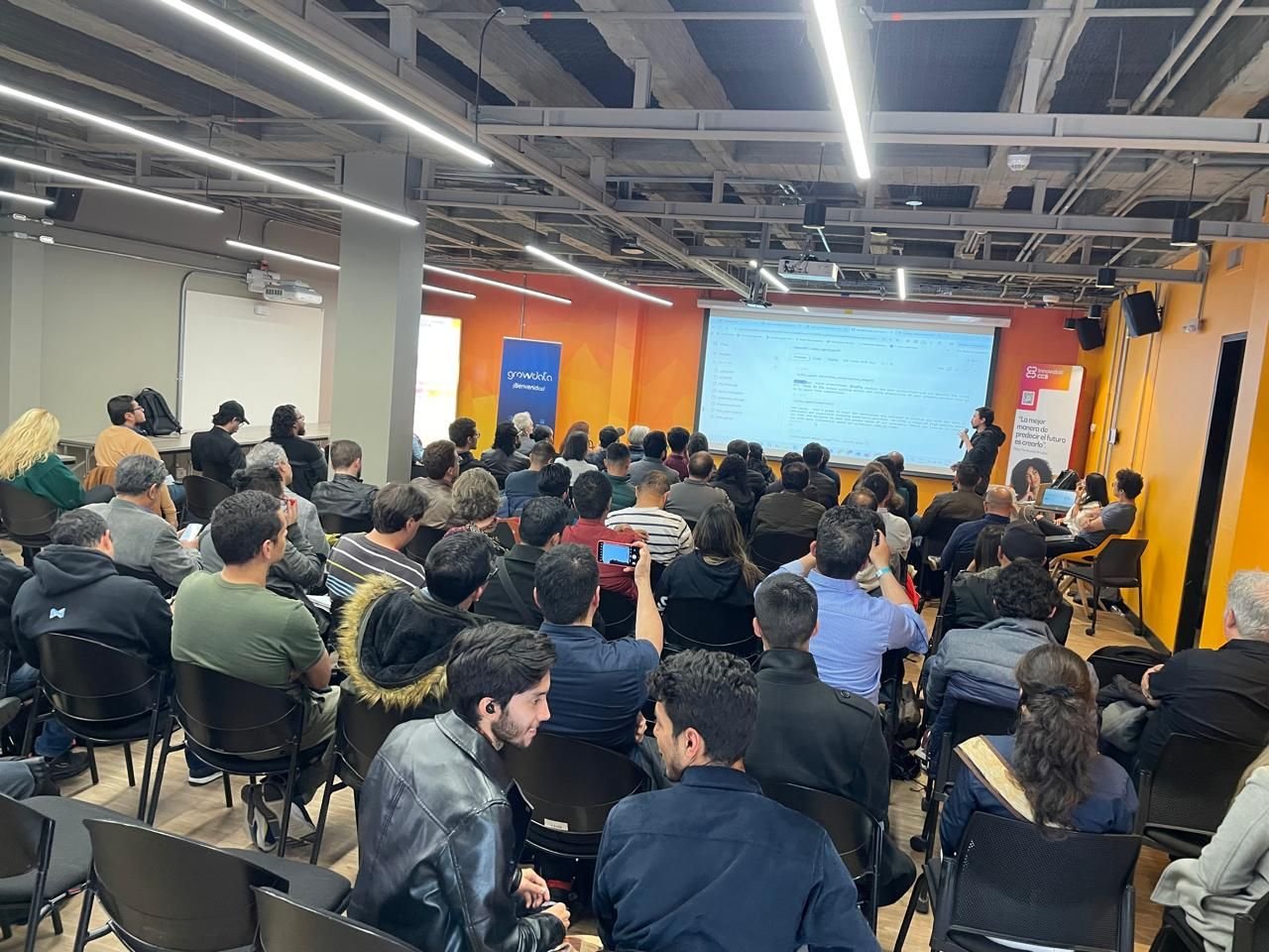 A photo of a large group of people attending a presentation in a modern conference room.