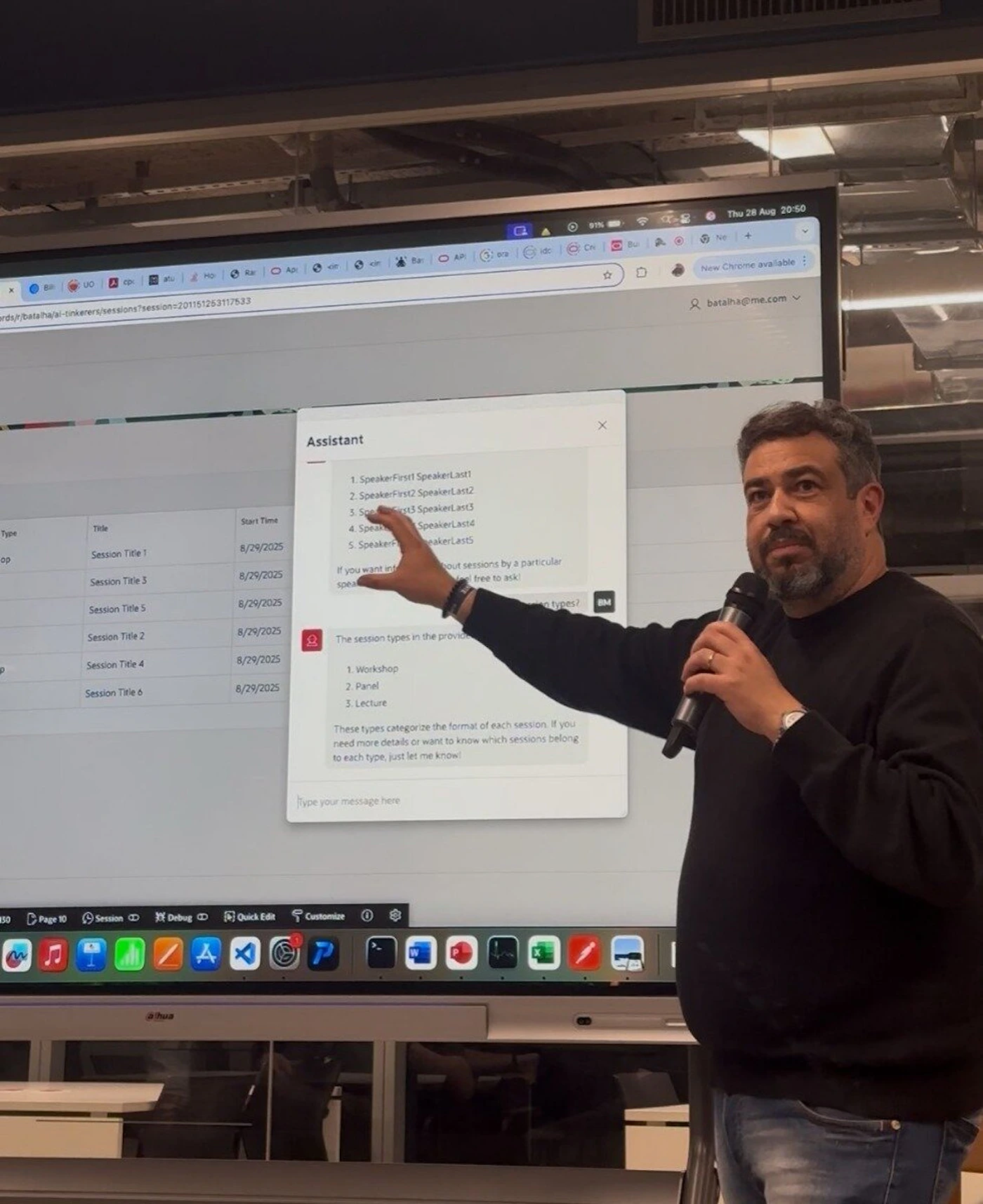 (Photo) A man with a beard, wearing a dark sweater and jeans, is presenting in an indoor setting, holding a microphone and pointing at a large screen. The screen displays a web application interface with a table and a chat assistant overlay. Text: Thu 28 Aug 20:50 New Chrome available batalha@me.com batalha/ai-linker/sessions?session=201151263117633 Type Title Start Time Session Title 1 8/29/2025 Session Title 3 8/29/2025 Session Title 5 8/29/2025 Session Title 2 8/29/2025 Session Title 4 8/29/2025 Session Title 6 8/29/2025 Assistant 1. SpeakerFirst1 SpeakerLast1 2. SpeakerFirst2 SpeakerLast2 3. SpeakerFirst3 SpeakerLast3 4. SpeakerFirst4 SpeakerLast4 5. SpeakerFirst5 SpeakerLast5 If you want information about sessions by a particular speaker, feel free to ask! The session types in the provide 1. Workshop 2. Panel 3. Lecture These types categorize the format of each session. If you need more details or want to know which sessions belong to each type, just let me know! Type your message here Page 10 Session Debug Quick Edit Customize ahwa person, digital display, presentation | indoor, conference room or similar | man holding a microphone, pointing at a large interactive screen, screen displaying a user interface with text and a chat assistant, various application icons on a dock/taskbar | candid, presentation | Colors: #2C2C2C, #F0F0F0, #446688, #A07F69, #FF0000 Note: The image is a direct capture of a real-world scene, featuring a person and a physical environment, rather than a graphic design, illustration, or text document. It shows a moment from a presentation or meeting.
