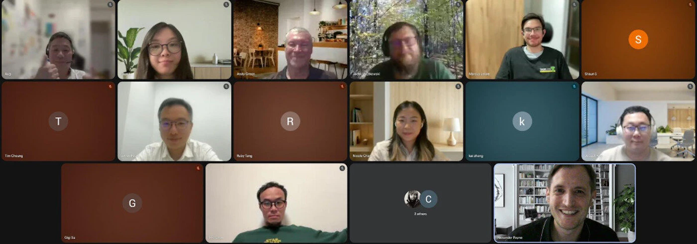 (Photo) A screenshot of a video conference call displaying 15 participants in a grid format, featuring a mix of live video feeds of people and profile initial placeholders on solid colored backgrounds. Text: Andy Green, Jozef Jaworski, Martin Cabot, Shaun S, Tim Cheung, Ruby Tang, Nicole Chan, Kai Zhang, Gigi Yu, C 2 others, Alexander Payne Multiple people participating in a digital meeting/video conference. | Digital interface (video conference grid), with various indoor and outdoor backgrounds visible in the individual feeds. | Grid layout of 15 panels (3x5), mix of visible cameras and initial avatars, names displayed underneath the feeds. | Screenshot, digital meeting capture. | Colors: #202124, #8d493a, #e67c29, #4a656a, #ffffff Note: The image is a screenshot capturing a video conference call, documenting the appearance and arrangement of multiple participants and their digital interface elements in a grid layout.