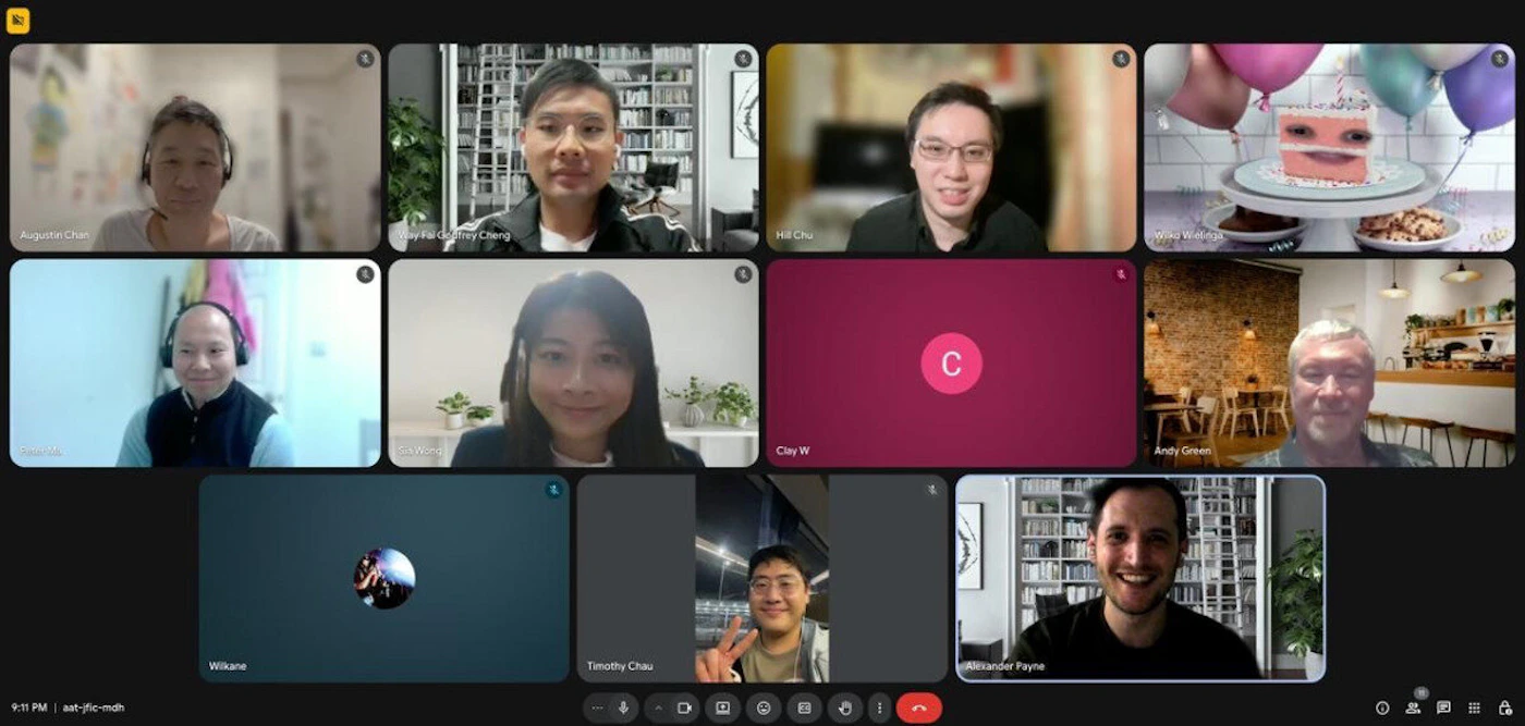 (Photo) A screenshot of a video conference call displaying twelve tiles in a grid layout, featuring several participants, one placeholder initial, and a humorous virtual background depicting a cake with eyes. Text: Augustine Chan Gay Fai Godfrey Cheng Hill Chu Winky Winky Lisa Wong C Clay W Andy Green Wilkane Timothy Chau Alexander Payne 9:11 PM aat-jfic-mdh Multiple people participating in a video conference/online meeting. | Virtual/online meeting environment (screenshot of a computer interface). | Grid layout of 12 tiles; names displayed below video feeds; one tile shows a surreal birthday cake background; dark interface design. | Screenshot, documentary style of a virtual event. | Colors: #1F1F1F, #FFFFFF, #9B1C4B, #008080 Note: The image captures a moment in time—a virtual meeting—and consists primarily of video feeds (photos) of people, documenting a real-world (or virtual) event.
