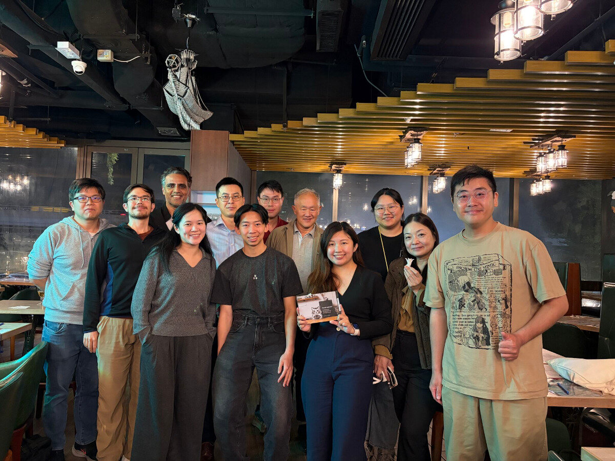 A group of twelve people posing for a group photo in what appears to be a restaurant or social venue with warm lighting.. Text: THE CAT MIMIC