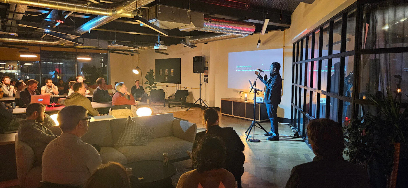 (Photo) A photo of a person giving a presentation or speech to a small audience in a dimly lit room. people | indoor | presentation, audience, dimly lit | candid Note: The image is a real-life captured scene of an event, depicting people and a setting, making it a photograph.
