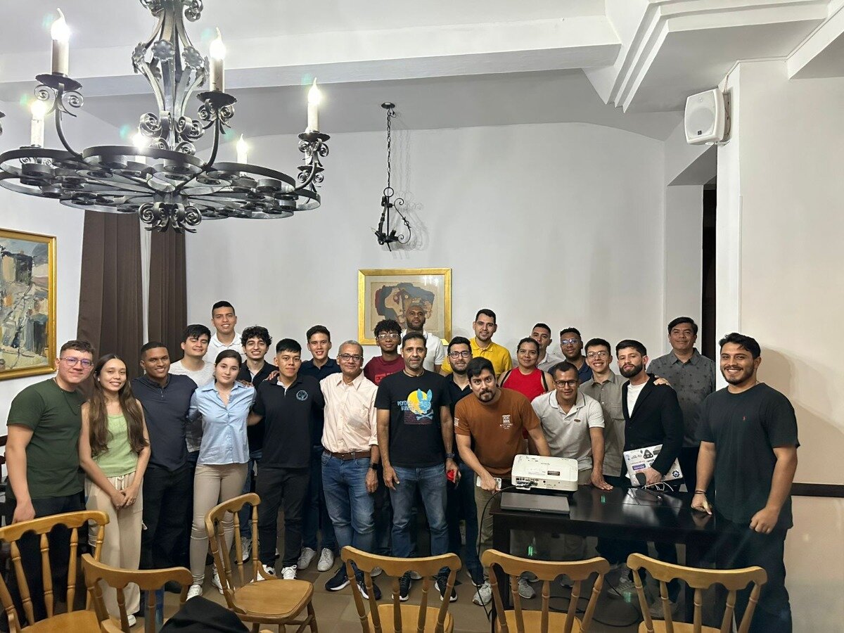 A group of people are posing for a photo in a room. They are standing and some are sitting at a table.
