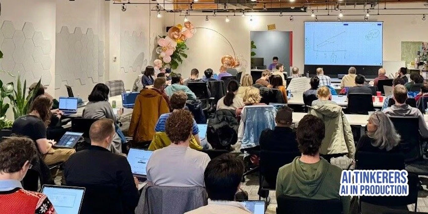 (Photo) A group of people are sitting in a room, looking at a presentation on a large screen. They appear to be attending a workshop or conference, with many using laptops. Text: AI TINKERERS AI IN PRODUCTION people | indoor | presentation, laptops, group of people | candid Note: The image is a real-life captured scene of an event, showing people and a presentation, making it a photograph.