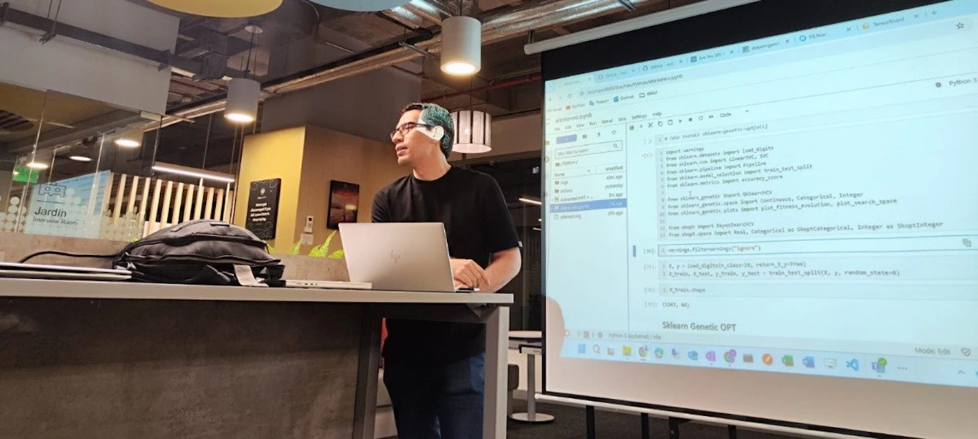 (Photo) A photo of a person giving a presentation about computer programming, with code projected on a screen. Text: from evalml.pipelines import LinearRegression from evalml.datasets import load_diabetes from evalml.preprocessing import split_data from evalml.model_selection import train_test_split from evalml.metrics import accuracy_score from evalml.automl import AutoMLSearch from evalml.genetic_opt import load_continuous, load_categorical, load_integer from evalml.genetic_opt import Algorithms from evalml.genetic_opt.plots import plot_fitness_evolution, plot_search_space from skopt import Space from skopt.space import Real, Categorical as SkoptCategorical, Integer as SkoptInteger  # warnings.filterwarnings("ignore", category=FutureWarning) X, y = load_diabetes(return_X_y=True) X_train, X_test, y_train, y_test = train_test_split(X, y, random_state=0)  [unreadable]  Stream Genetic OPT person | indoor | presentation, projector screen, code | candid Note: The image is a real-world photograph of a person presenting with a projected screen showing code.  It captures a moment in time and is not a drawn illustration, logo, or banner.