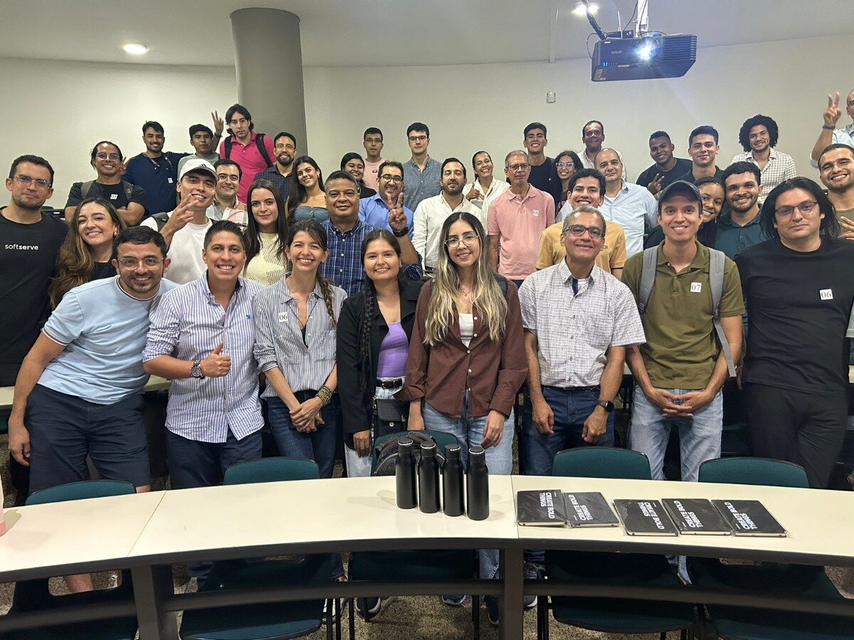 A large group of people poses for a photo in a lecture hall or classroom setting.  Several notebooks or pamphlets are laid out on the table in front of them.. Text: SOFTSERVE
CRAFT BEER
CRAFT BEER
CRAFT BEER
CRAFT BEER
CRAFT BEER
CRAFT BEER