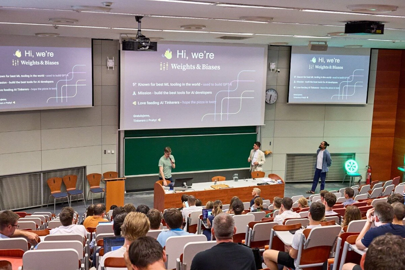 (Photo) A photo of a presentation in a lecture hall. The presentation is by Weights & Biases, and the audience is listening and watching. Text: Hi, we're Weights & Biases Known for best ML tooling in the wodddd Mission - build the best tools for AI developers Love feeding AI Tinkerers - hope the pizza is tasty Hi, we're Weights & Biases Hi, we're Weights & Biases people | indoor | presentation, audience, lecture hall | candid Note: The image is a real-life captured scene of a presentation, making it a photograph. It's not a logo, illustration, or other synthetic image type.