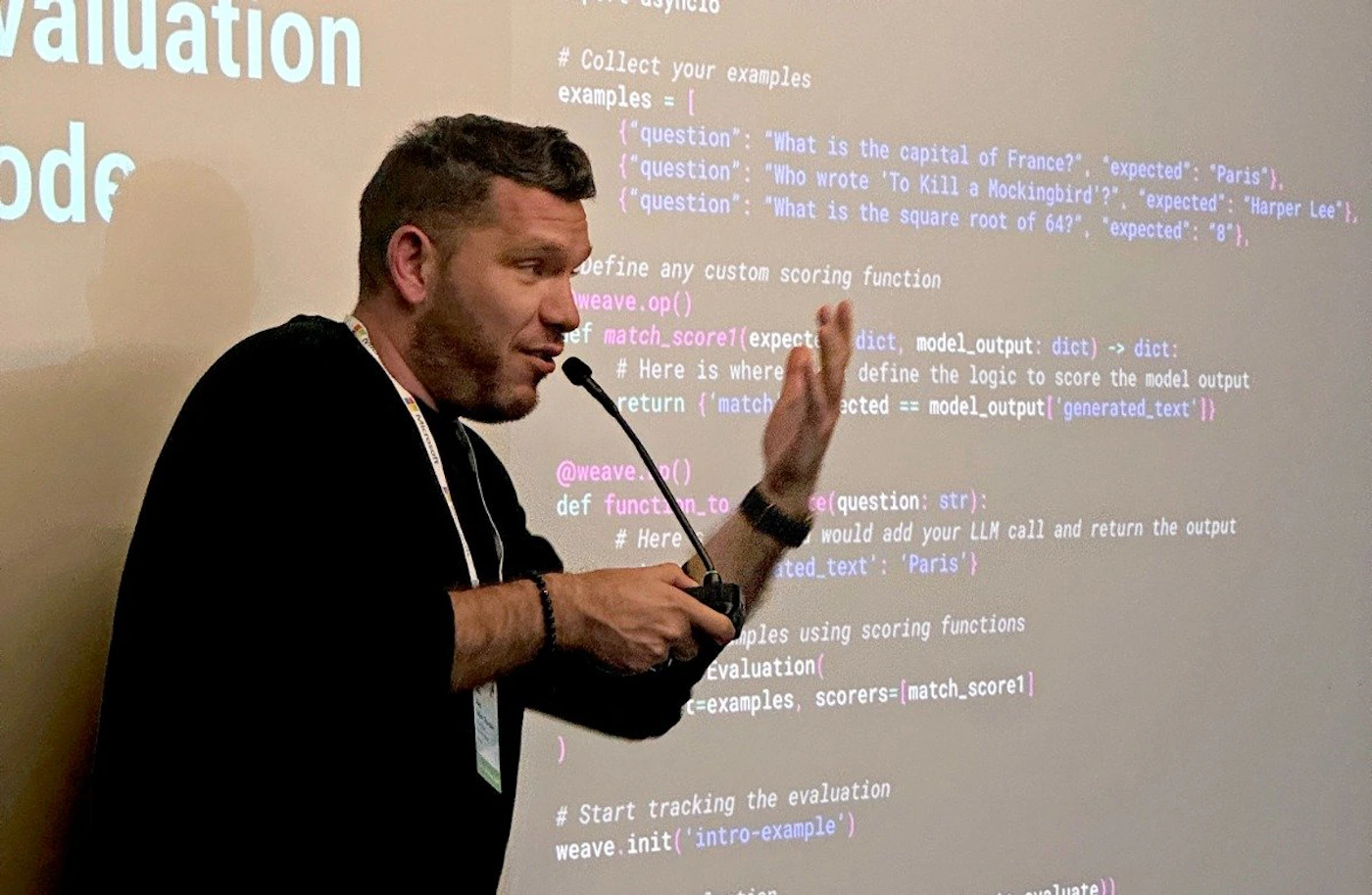 (Photo) A man in a black shirt is presenting, gesturing with his hand towards a projected screen displaying code examples and explanations. Text: Valuation ode # Collect your examples examples = [ {"question": "What is the capital of France?", "expected": "Paris"), {"question": "Who wrote 'To Kill a Mockingbird'?", "expected": "Harper Lee"}, {"question": "What is the square root of 64?", "expected": "8"}, define any custom scoring function weave.op() ef match_scorel(expecte dict, model_output: dict) -> dict: #Here is where return {'match @weave.() def functn to # Here define the logic to score the model output acted == model_output['generated_text']} ce(question: str): would add your LLM call and return the output ated_text': 'Paris'} aples using scoring functions Evaluation( c=examples, scorers=[match_score1] #Start tracking the evaluation weave.init('intro-example') luate person | indoor | projected code, presentation | candid Note: The image is a photograph of a person presenting code on a projector screen. It captures a real-life scene, making "photo" the most appropriate category.