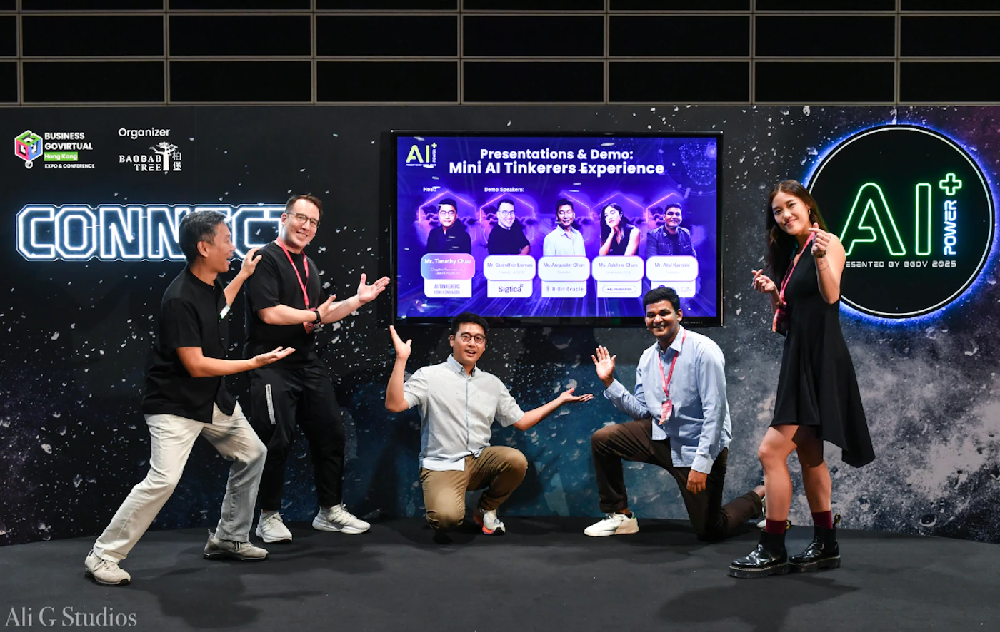 (Photo) A group of six individuals, five men and one woman, are enthusiastically posing in front of a large digital screen and a dark, patterned backdrop at what appears to be an event or conference. The screen displays a presentation title and speaker details, while the backdrop features event branding and logos. Text: BUSINESS GOVIRTUAL HONG KONG EXPO & CONFERENCE Organizer BAOBAB TREE CONNECT AI Presentations & Demo: Mini AI Tinkerers Experience Host: Demo Speakers: Mr. Timothy Chan AI INNOVATION Mr. Gaurav Loria Signtool Mr. Jagadeesh Chan T-HUB INDIA Ms. Adarsh Chan AI POWER Mr. Atul Karde AI INNOVATION AI+ POWER PRESENTED BY BGOV 2025 Ali G Studios group of people, event, technology conference | indoor, event booth/stage | six people posing, large digital display showing presentation details, event branding on the backdrop, glowing text elements | posed, promotional, event photography | Colors: #1A1A1A, #00FFFF, #FFFFFF, #222222, #F0F0F0 Note: This image is a direct capture of a real-world scene featuring people and an event setting, which is characteristic of a photograph. It documents an activity rather than being a designed graphic, logo, or hand-drawn content.