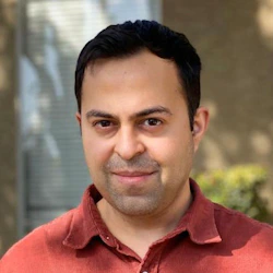 (Photo) A headshot photo of a man with dark hair and a reddish-orange collared shirt. person | outdoor | headshot | portrait Note: The image is a real-life captured image of a person, making it a photograph.  It doesn't contain any text or design elements to suggest other categories.