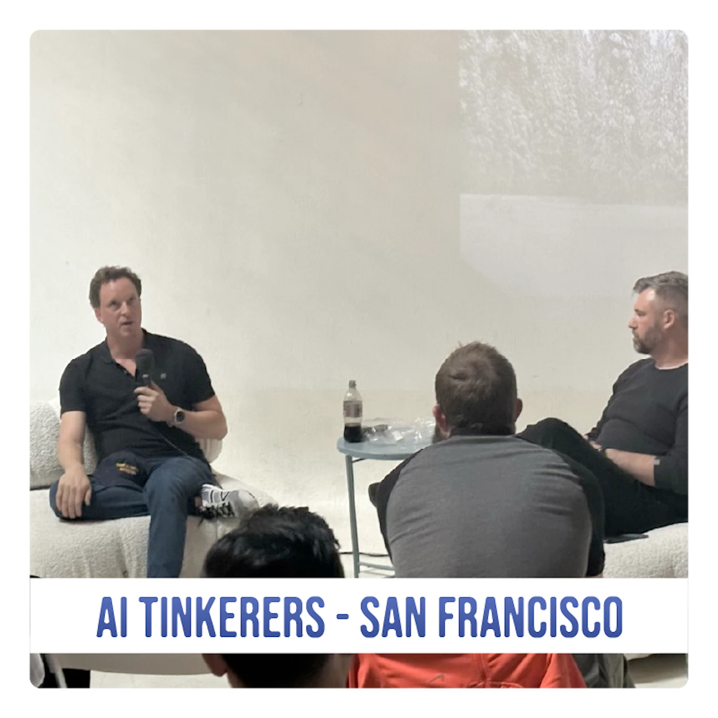 (Photo) A photo of a man speaking to a small audience in a casual setting. The event appears to be related to AI Tinkerers in San Francisco. Text: AI TINKERERS - SAN FRANCISCO people | indoor | small group, presentation | candid Note: The image is a real-life captured image of people in a room, making it a photograph.  The added text banner further suggests it's documenting an event.