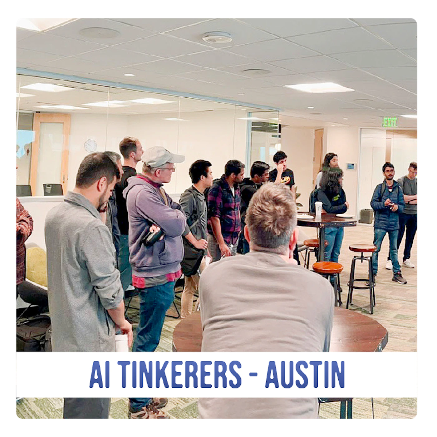 (Photo) A photo of a group of people gathered in a room, likely for a meeting or presentation. Text: AI TINKERERS - AUSTIN people | indoor | group of people, presentation/meeting setting | candid Note: The image is a real-life captured image of people in a room, making it a photograph. The text banner at the bottom suggests it documents an event.