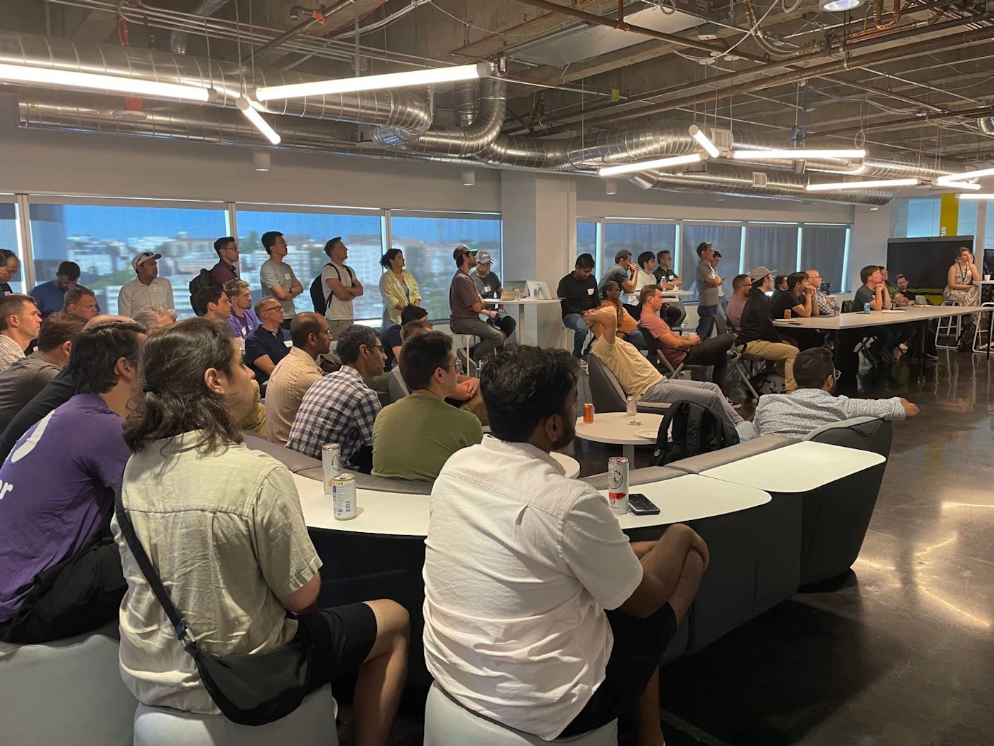 (Photo) A photo of a group of people sitting in a modern office space, seemingly attending a presentation or meeting. people | indoor | group of people, office setting, presentation/meeting | candid Note: The image is a real-life captured image of a scene with people in an office setting, indicative of a photograph.