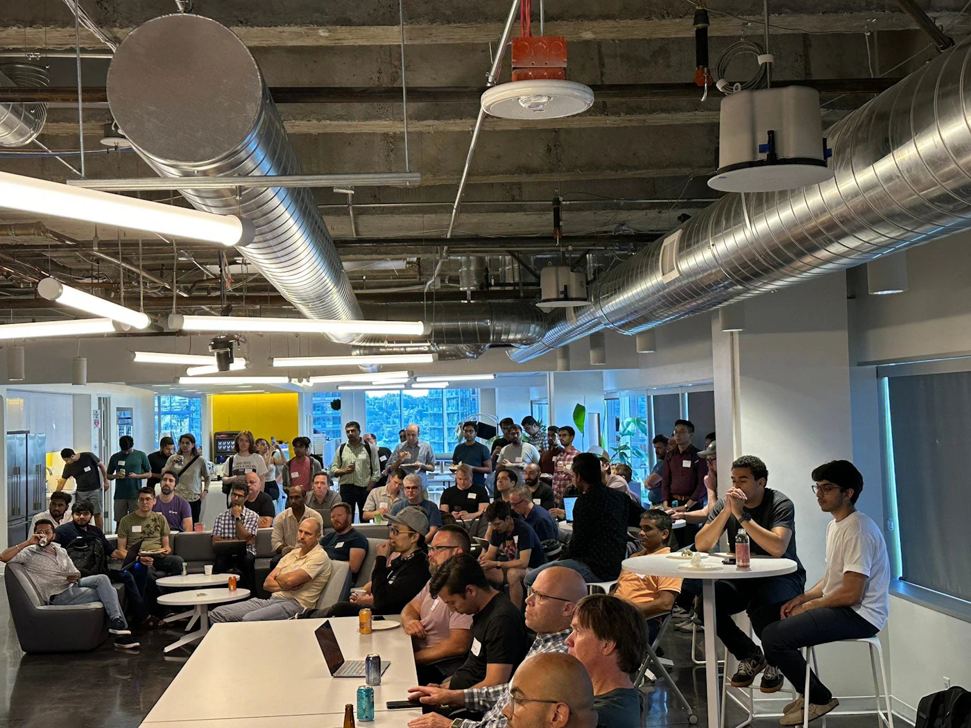 (Photo) A photo of a large group of people gathered in a modern office space, likely for a presentation or meeting. people | indoor | large group, office setting, presentation/meeting | candid Note: The image is a real-life captured scene of people in an office environment, indicative of a photograph. It doesn't contain any specific branding or artistic elements to categorize it as a logo or illustration.