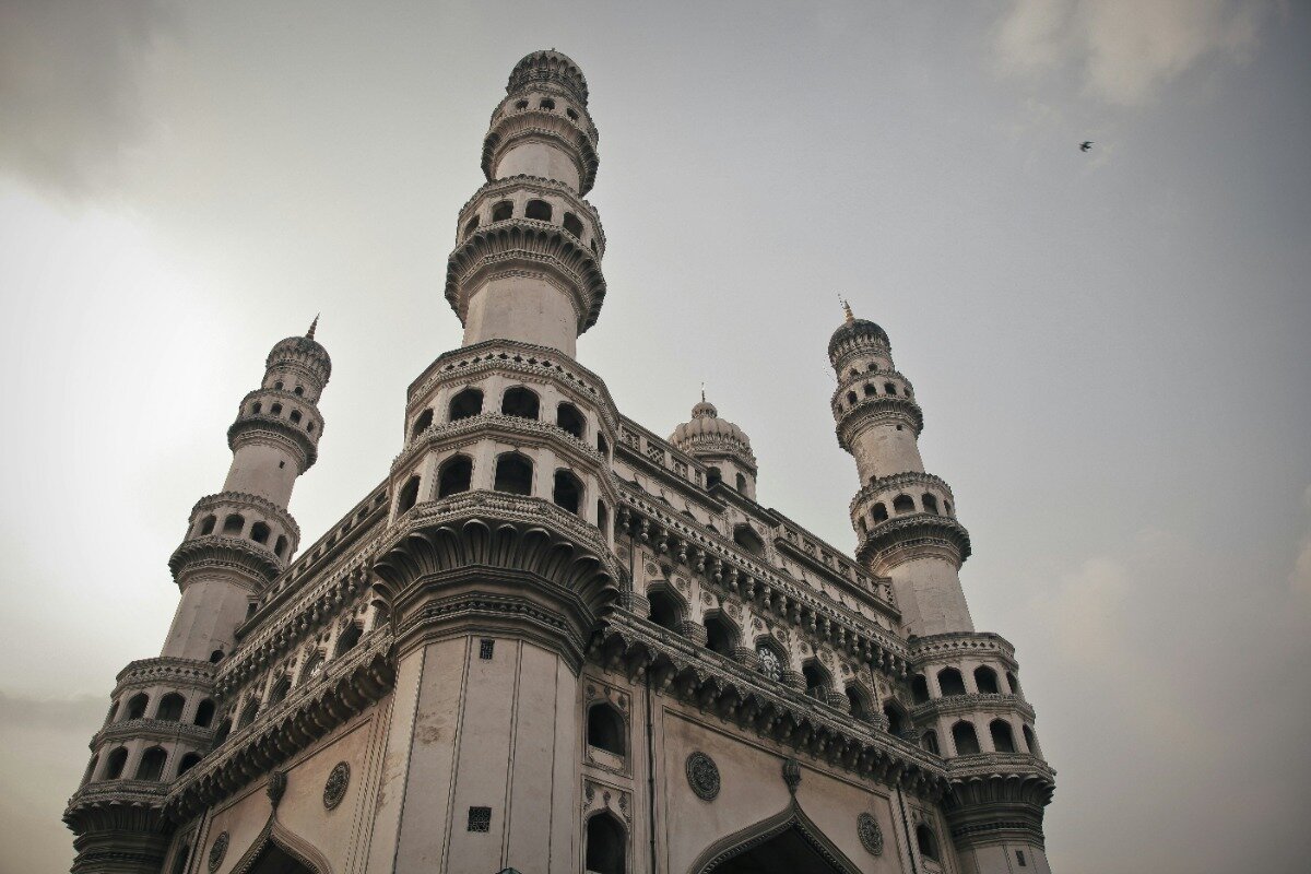 A low-angle photo of the Charminar, a monument and mosque located in Hyderabad, India.  The four minarets are prominent against the sky.