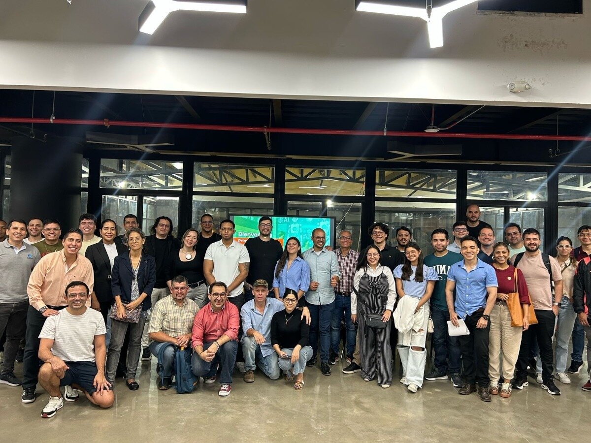 A group of people is posing for a photo inside a building. They are standing and sitting in multiple rows, looking at the camera.. Text: Bienven