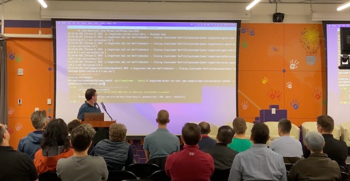 (Photo) A photo of a presenter speaking to an audience in a room.  A projected screen displays lines of code. Text: 07:34:48.456 [Thread-12] INFO lang.thread.ShutdownHook - Shutdown hook 07:34:48.456 [Thread-12] INFO lang.api.NetFileClassLoader - Closing classloader NetFileClassLoader(name= "langstream-agent") 07:34:48.456 [Thread-12] INFO lang.api.NetFileClassLoader - Closing classloader NetFileClassLoader(name= "langstream-agent") 07:34:48.456 [Thread-12] INFO lang.api.NetFileClassLoader - Closing classloader NetFileClassLoader(name= "langstream-agent") 07:34:48.456 [Thread-12] INFO lang.api.NetFileClassLoader - Closing classloader NetFileClassLoader(name= "langstream-agent") processing 2007, a Langstream doc run test - eops example/applications/docs/onboarding 5 user docs, 2 query docs, 0 primary to answer 4.1 sec derivation (157) 07:34:52.611 [Thread-12] INFO lang.api.NetFileClassLoader - Closing classloader NetFileClassLoader(name= "langstream-agent") 4.1 sec derivation (157) 07:34:52.611 [Thread-12] INFO lang.api.NetFileClassLoader - Closing classloader NetFileClassLoader(name= "langstream-agent") 4.1 sec derivation (157) 07:34:52.611 [Thread-12] INFO lang.api.NetFileClassLoader - Closing classloader NetFileClassLoader(name= "langstream-agent") 4.1 sec derivation (157) 07:34:52.611 [Thread-12] INFO lang.api.NetFileClassLoader - Closing classloader NetFileClassLoader(name= "langstream-agent") springfox.swagger2.DerivableList@133.nor? Closing environment (yarn run workspace @aws-amplify/e2e-tests repo:list --json) | jq '.repositories[] | select(.name == "@aws-amplify/e2e-tests")' | jq -r '.location' cd "$REPO_DIR" yarn install --frozen-lockfile yarn test:e2e --filter docs-onboarding-e2e --verbose Docs are kept in a read-only dir, and primarily in answer... Welcome to (volume 1)  people | indoor | presentation, audience, code projection | candid Note: The image captures a real-life scene of a presentation, making it a photograph.  It's not a logo, banner, illustration, or handwriting.