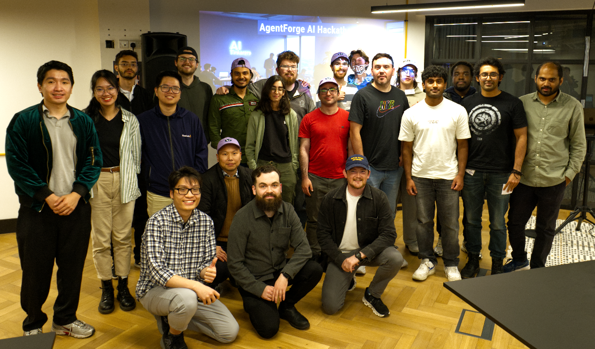 (Photo) A group of approximately 20 young adults, predominantly men, are posing for a photo indoors, likely at an event or hackathon. A large screen behind them displays text related to an 'AgentForge AI Hackathon'. Text: AgentForge AI Hackath AI group of people | indoor, event space | multiple people, projected screen with text, some individuals wearing hats, diverse group | group portrait, candid | Colors: #D2B48C, #F5F5DC, #2F4F4F, #000000, #FFFFFF, #800080 Note: The image is a direct capture of a real-world scene featuring a group of people, which is characteristic of a photograph. It is not an illustration, logo, banner, or handwriting.