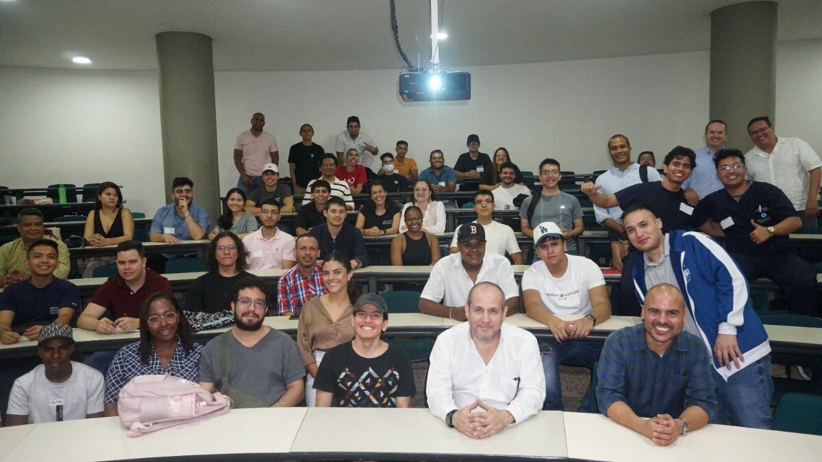 A group of people are sitting in a lecture hall or classroom, possibly for a training session or conference.