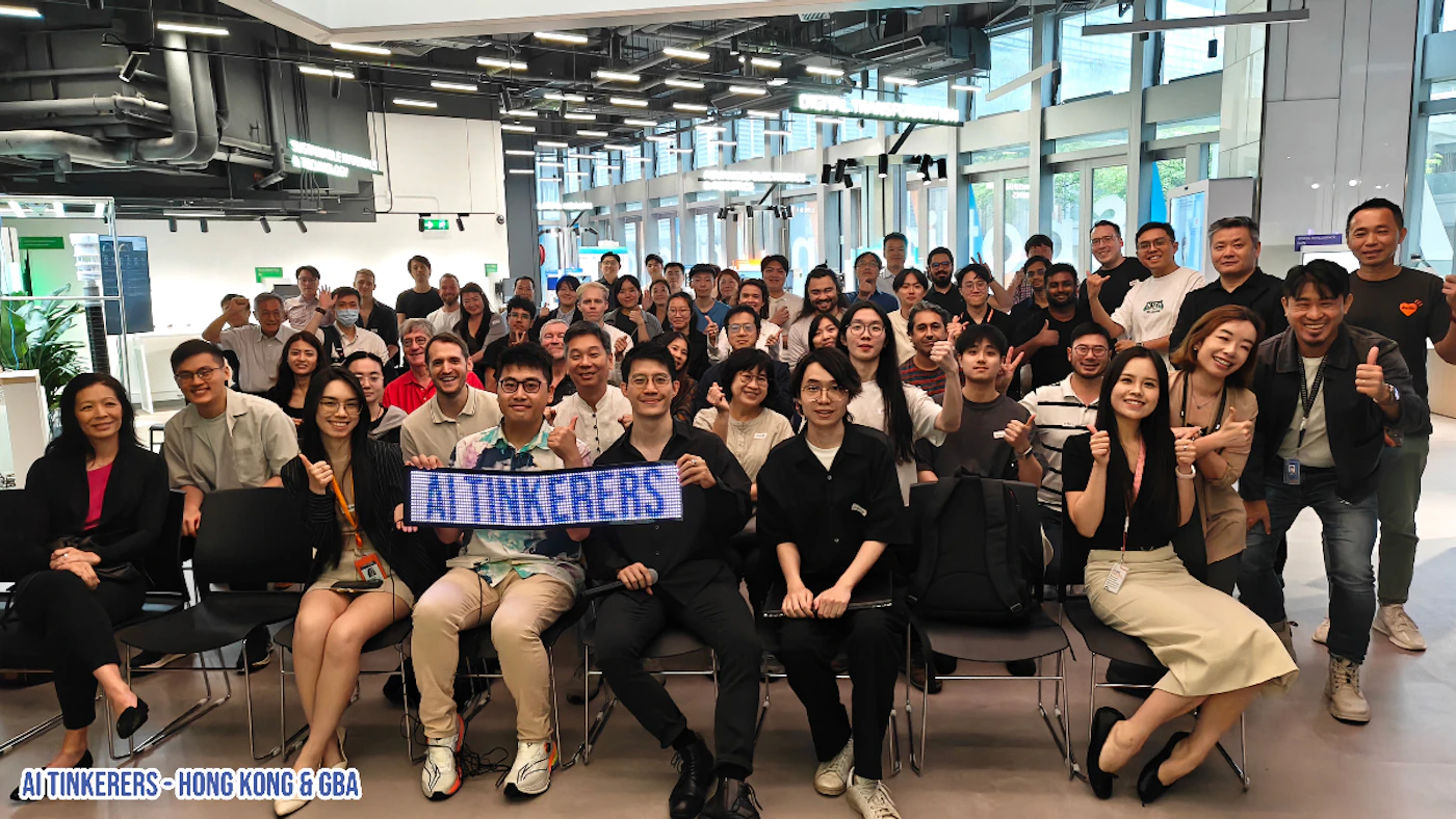 (Photo) This is a photo of a large group of people posing for a picture indoors. Many are giving a thumbs-up, and some are holding a sign that says 'AI TINKERERS'. Text: AI TINKERERS AI TINKERERS - HONG KONG & GBA group of people | indoor | large group, sign with text, thumbs-up gestures | candid | Colors: #FFFFFF, #000000, #C0C0C0 Note: The image shows a real-world scene with people, making it a photograph. It's not a logo, banner, illustration, or handwriting sample.