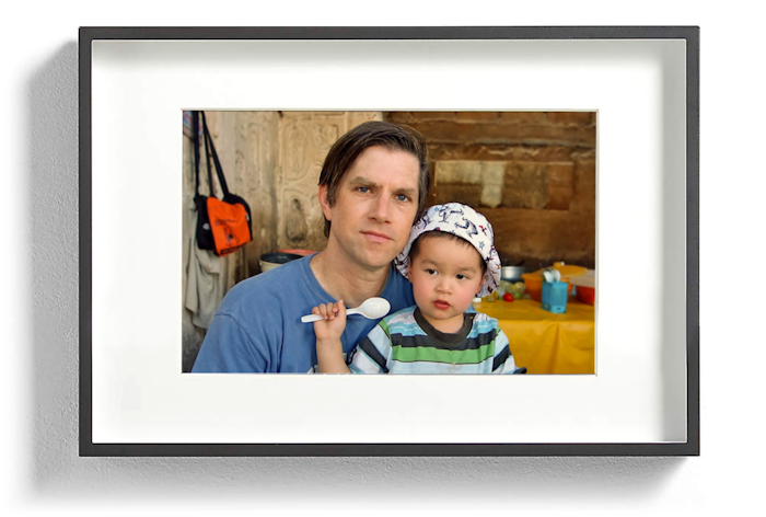 A photo of a man holding a young child. The child is holding a spoon.