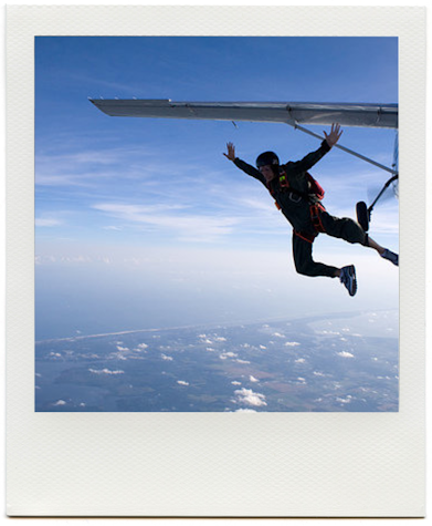 A photo of a person skydiving out of a plane, high above the ground.