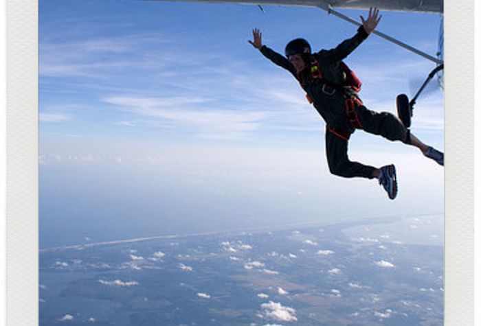 A photo of a person skydiving out of a plane, high above the ground.