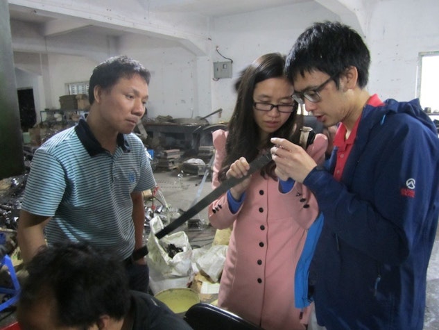 Three people are examining a long, dark object in what appears to be a workshop or factory setting.