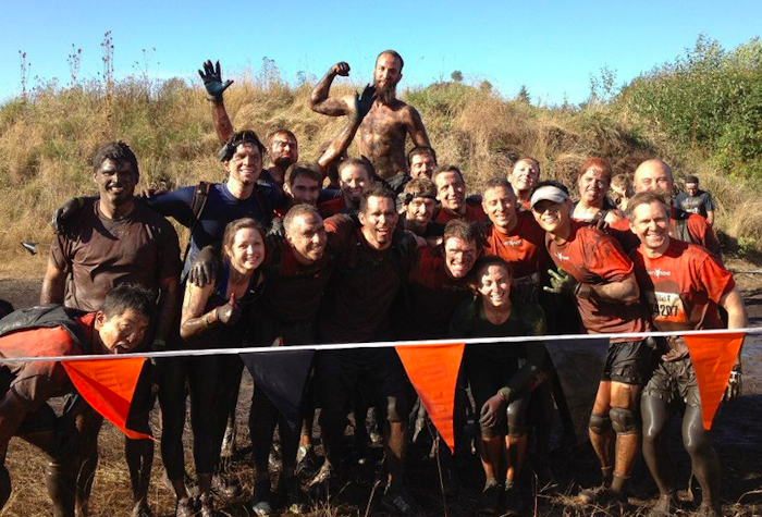 A group of people covered in mud pose for a photo after a mud run.