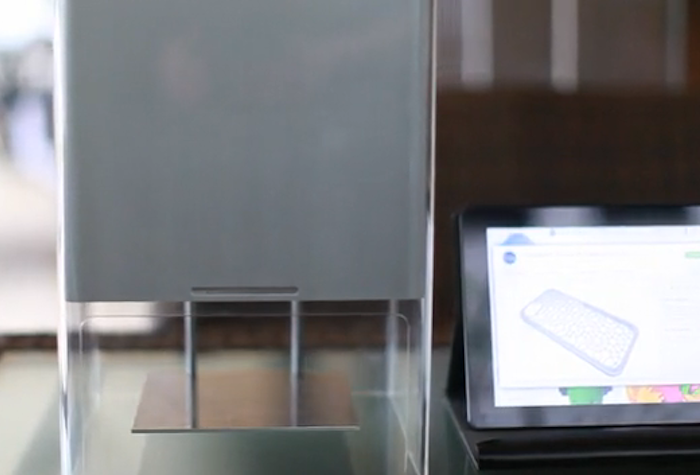 A photo of a 3D printer next to a tablet displaying a 3D model.