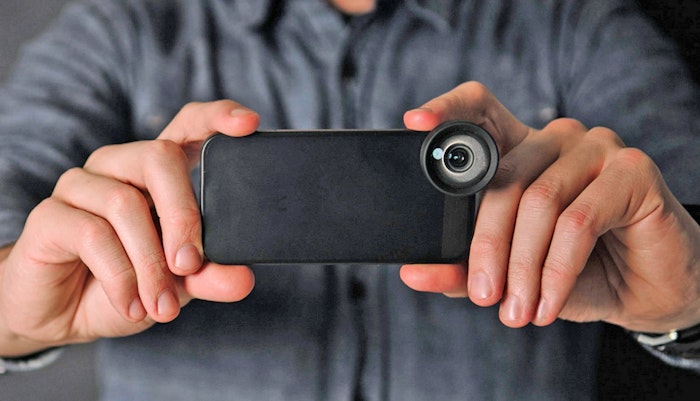 A person is holding a smartphone horizontally with an external lens attached.