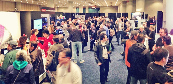 A photo of a crowded convention hall with people gathered around booths and displays.