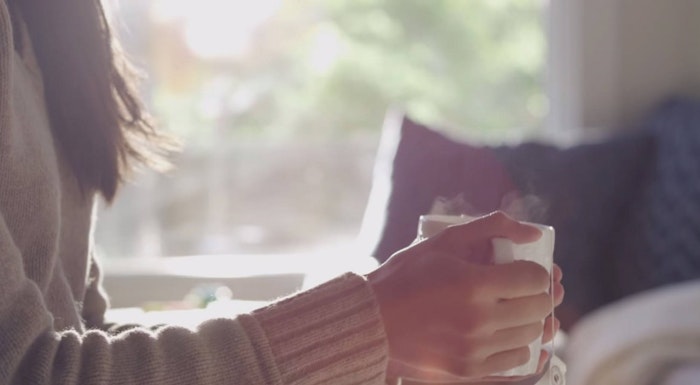 A person wearing a sweater is holding a steaming mug, likely enjoying a warm beverage.