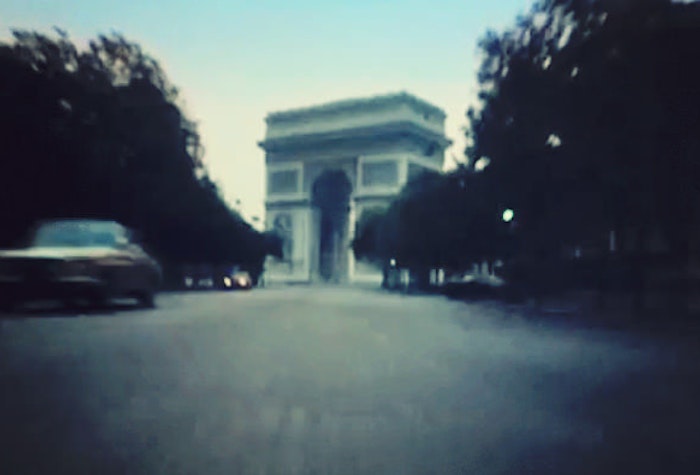 A blurry photo of the Arc de Triomphe in Paris, taken from a low angle, with a car in the foreground.