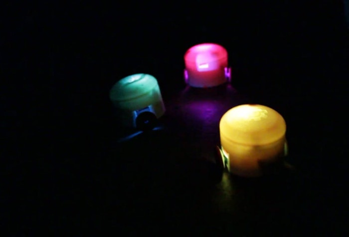 A photo of three small, glowing objects in a dark environment. They appear to be small lights or LEDs, each emitting a different color.