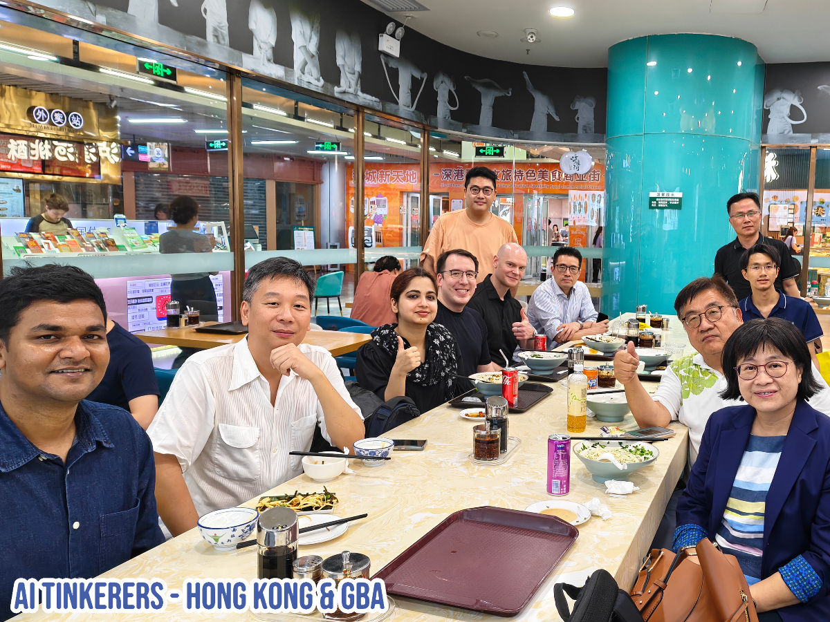 (Photo) A group of people are sitting around a table in what appears to be a restaurant, posing for a photo. They are smiling and giving thumbs up. Text: AI TINKERERS - HONG KONG & GBA group of people | indoor | multiple people, restaurant setting | candid | Colors: #FFFFFF, #000000, #C0C0C0 Note: The image shows a real-world scene with people and objects, which is typical of a photograph. The presence of people and a restaurant setting further supports this classification.