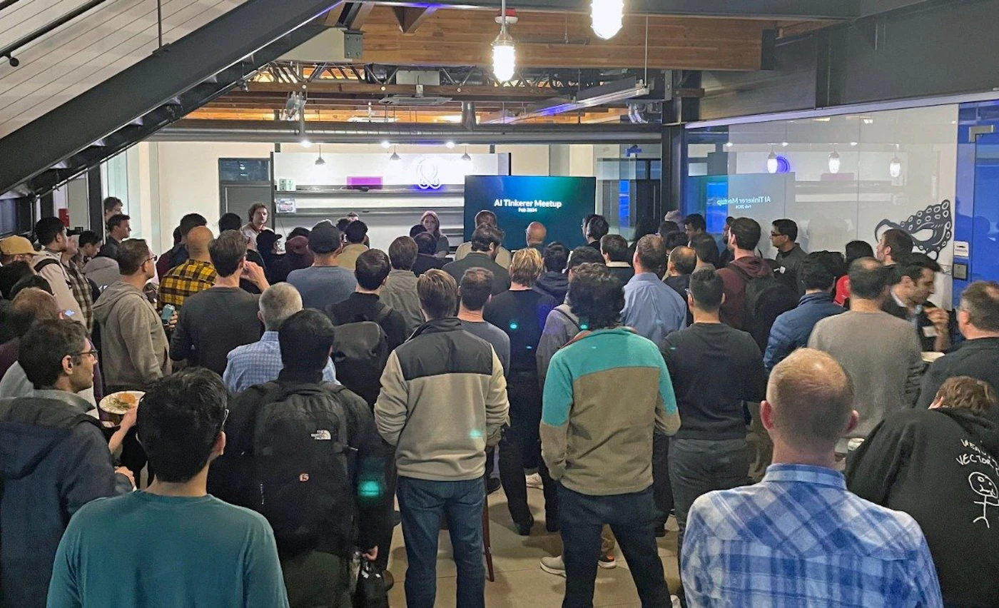 (Photo) A photo of a large group of people gathered in a room, seemingly attending a presentation or meeting. Text: AI Tinkerer Meetup people | indoor | large group, presentation screen | candid Note: The image is a real-life capture of an event, depicting people and a setting.  It's not a drawing, logo, or banner.