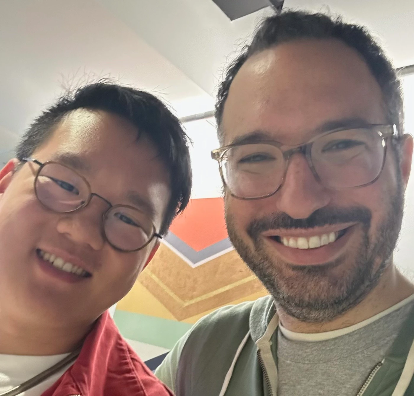 (Photo) A selfie photo of two people smiling at the camera. person | indoor | two people, selfie | selfie Note: The image is a real-life captured image of two people, clearly a photograph, not a drawing or other type of image.