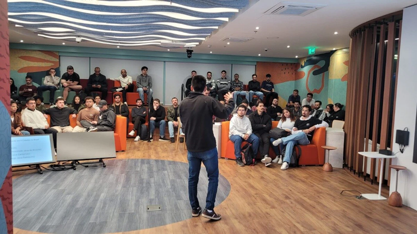 (Photo) A photograph captures an indoor gathering where a person is speaking to an audience seated on couches and chairs in a modern room. The room features wood flooring, colorful wall murals, and a distinctive wave-patterned ceiling. Text: Um [unreadable] em [unreadable] no Brasil Uma [unreadable] Criação [unreadable] Melhoria [unreadable] Nova [unreadable] A presentation or meeting with a speaker and an audience. | Indoor, a modern event or meeting room. | A speaker addressing an audience, multiple people, a large screen displaying text, contemporary interior design with diverse seating options. | Candid, event photography. | Colors: #8B4513, #FF4500, #40E0D0, #F5F5F5 Note: The image is a direct capture of a real-world scene, featuring people and an environment, which is the defining characteristic of a photograph.