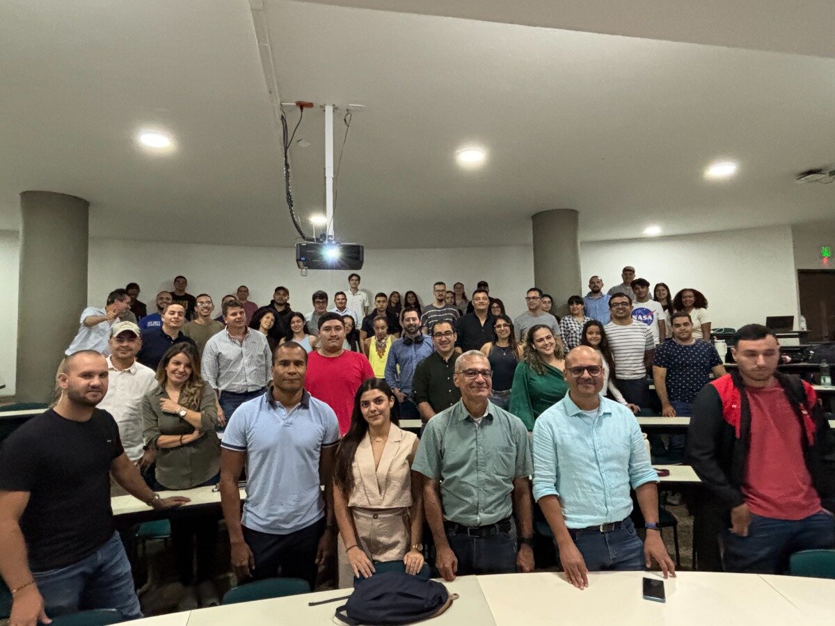 A group of people are posing for a photo in what appears to be a classroom or lecture hall. There is a projector hanging from the ceiling.. Text: NASA