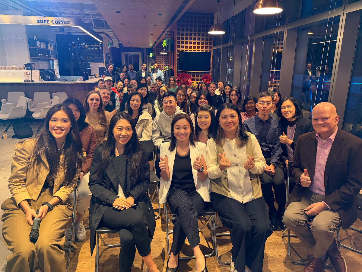 A large, diverse group of people posing for a group photograph in a modern indoor office or lounge setting with a coffee bar in the background.. Text: SOFE COFFEE