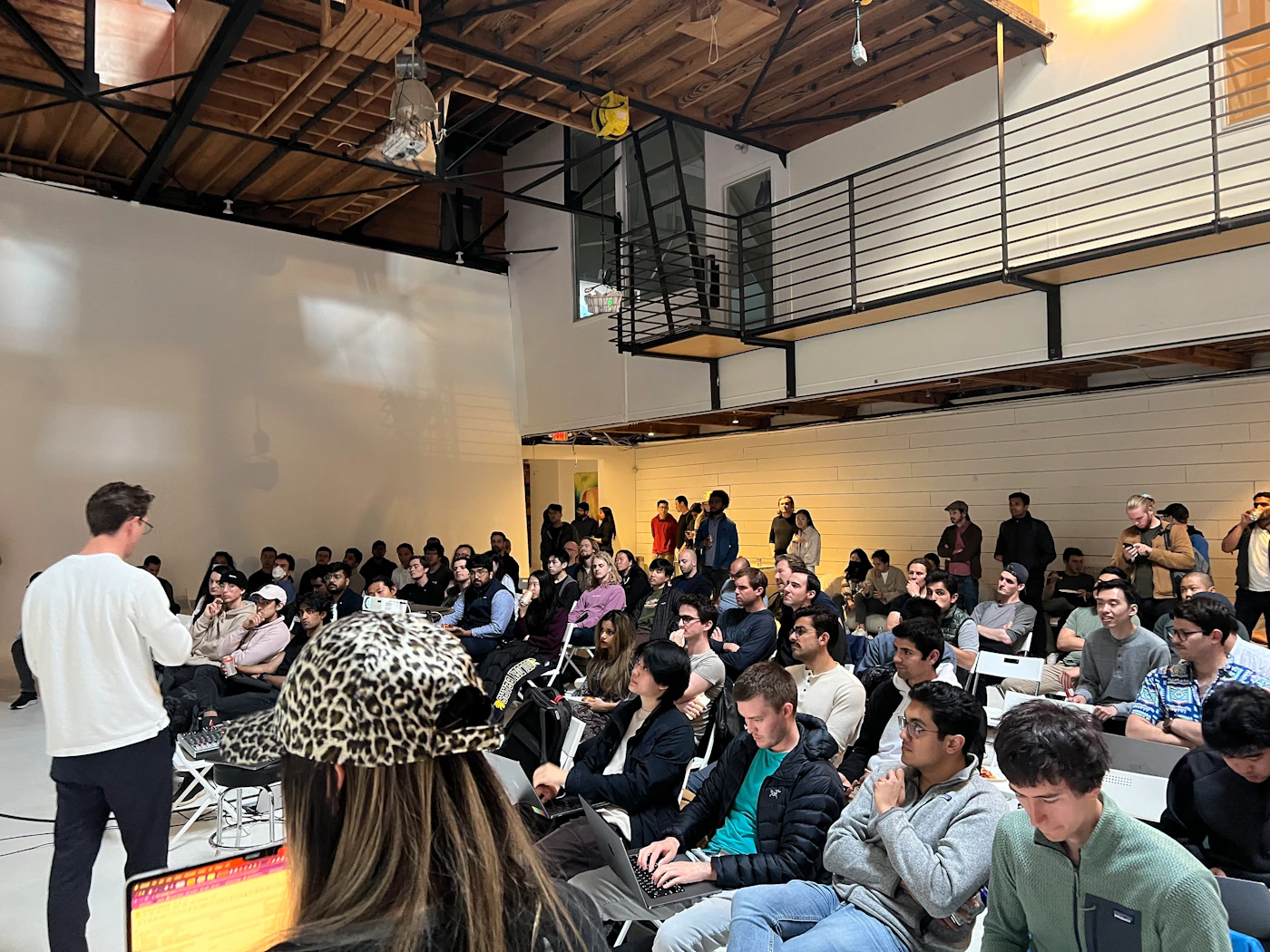 (Photo) A photo of a person presenting to a seated audience in a large room with a high ceiling. people | indoor | presentation, audience | candid Note: The image is a real-life captured image of a scene with people, making it a photograph.  It's not a logo, illustration, or other specific type.