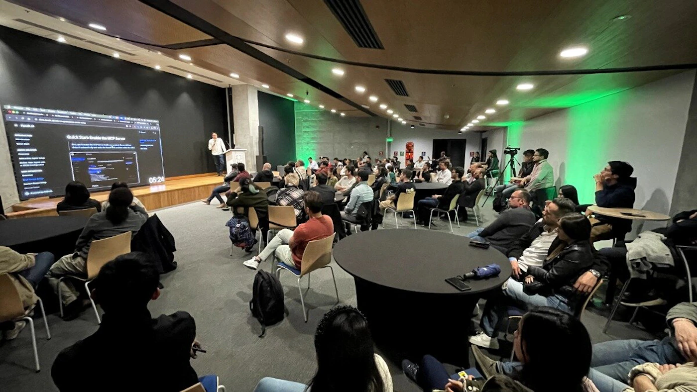 (Photo) The image shows a presentation in a large room with an audience. A person is standing on a stage presenting something displayed on a large screen. Text: Quick Start Guide to HCP Server 05:24 presentation, audience | indoor | large screen, stage, audience | candid | Colors: #000000, #FFFFFF, #808080 Note: The image is a real-world scene captured with a camera, making it a photograph. It depicts a presentation setting with people and a screen.