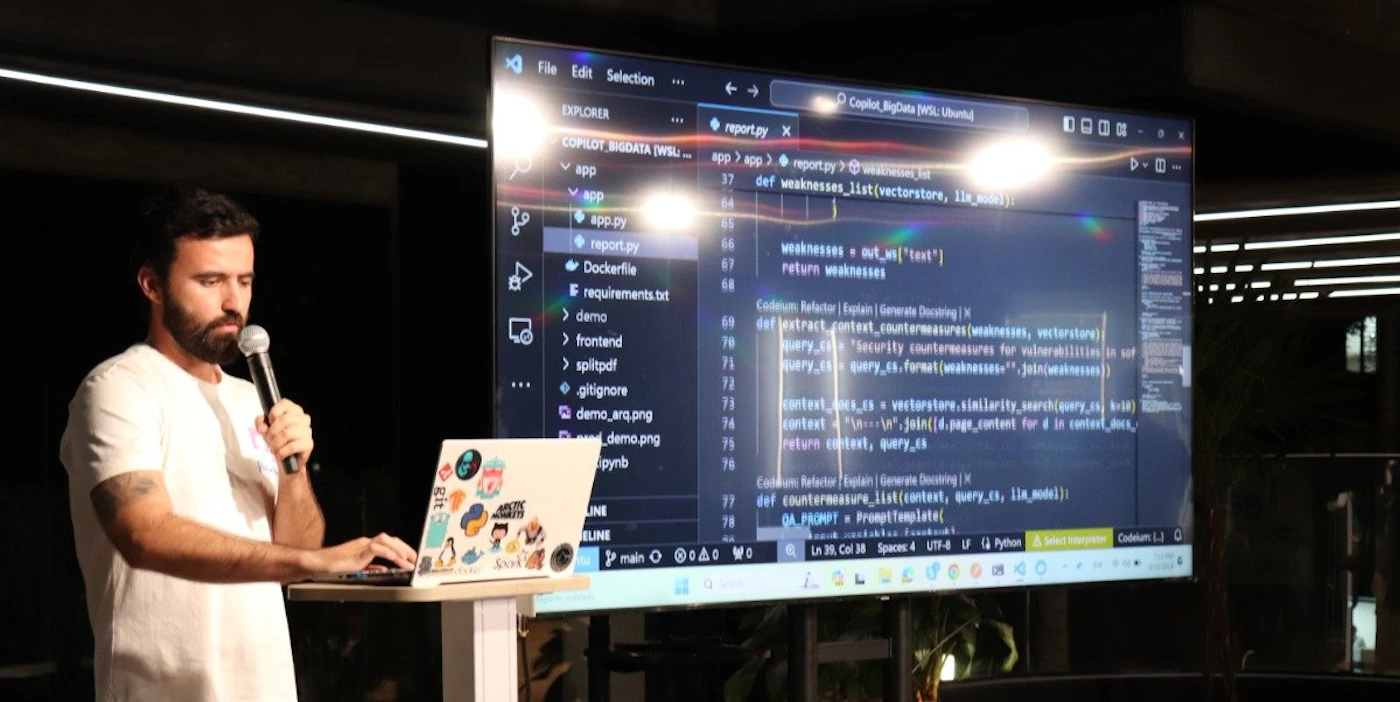 (Photo) A man is presenting, using a laptop and a large screen displaying code. Text: File Edit Selection EXPLORER Copilot BigData [WSL ...] app > app > report.py > w... app app.py report.py Dockerfile requirements.txt demo frontend splitpdf .gitignore demo_arq.png demo.png ... pynb ... 37 def weaknesses_list(vectorstore, lis_docs): ... 66 67     weaknesses = out_ws["text"] 68     return weaknesses ... 69 Codelum Reactor | Explain | Generate Docs 70 def extract_context_countermeasures(weaknesses, vectorstore): 71     query = "Security countermeasures for vulnerabilities in {0}" 72     query = query.format(weaknesses.join(weaknesses)) 73     context_docs = vectorstore.similarity_search(query, k=8) 74     context = "".join([d.page_content for d in context_docs]) 75     return context, query ... 76 Codelum Reactor | Explain | Generate Docs 77 def countermeasure_list(prompt_template, llm_model): 78     QA_PROMPT = PromptTemplate( ... Ln 26, Col 34 Spaces: 4 UTF-8 LF Python person | indoor | presentation, laptop, code on screen | candid Note: The image is a real-world photograph of a person giving a presentation involving code. It captures a moment in time and is not a digitally created illustration, logo, or banner.