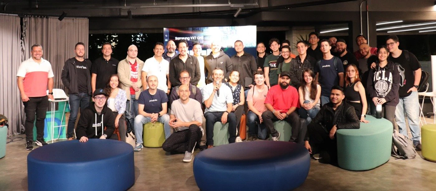 (Photo) A group of people are posing for a photo, likely at a company or social event. They are standing and sitting in multiple rows, some on colorful ottomans. people | indoor | group photo, multiple people | candid Note: The image is a real-life captured moment of a group of people, making it a photograph. It doesn't contain any designed elements to classify it as a logo, banner or illustration.