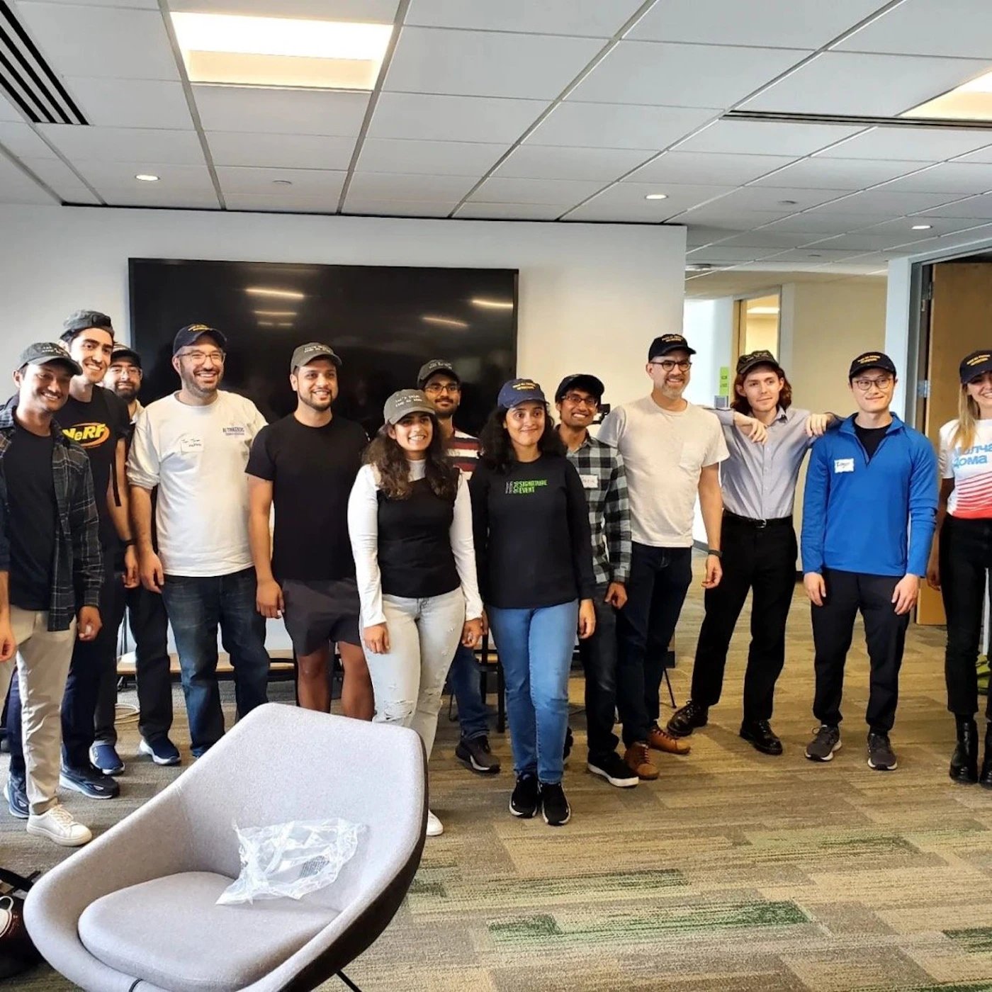 (Photo) A group of people wearing matching hats are standing together for a photo in an office setting. Text: NoRt people | indoor | group photo, matching hats | candid Note: The image is a real-life captured moment of a group of people, clearly a photograph, not a digitally created image or a logo.