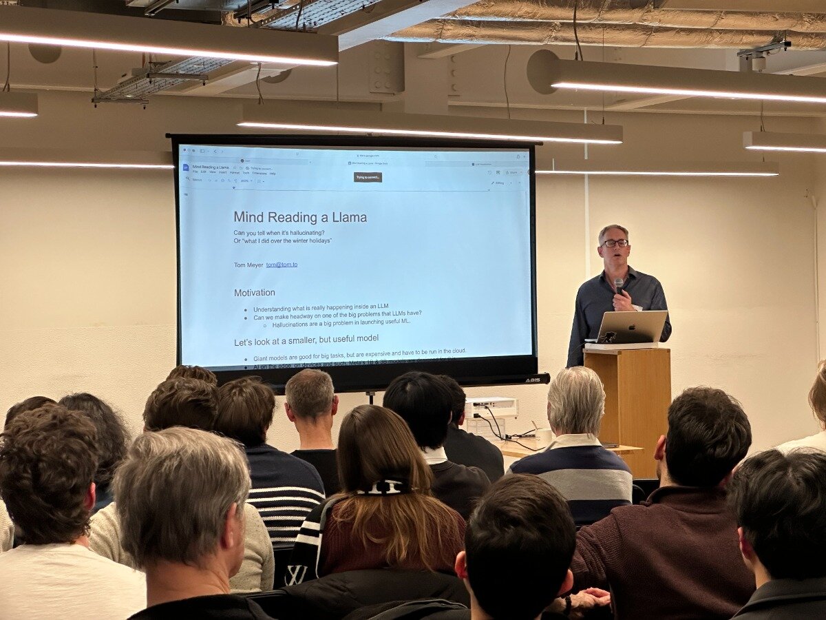 A man is presenting a talk titled "Mind Reading a Llama" to an audience in a conference room. The presentation slide is projected on a screen behind him.. Text: Mind Reading a Llama
Can you tell when it's hallucinating?
Or "what I did over the winter holidays"
Tom Meyer
Motivation
Understanding what is really happening inside an LLM
Can we make headway on one of the big problems that LLMs have?
Hallucinations are a big problem in launching useful LLMs.
Let's look at a smaller, but useful model
Giant models are good for big tasks, but are expensive and have to be run in the cloud