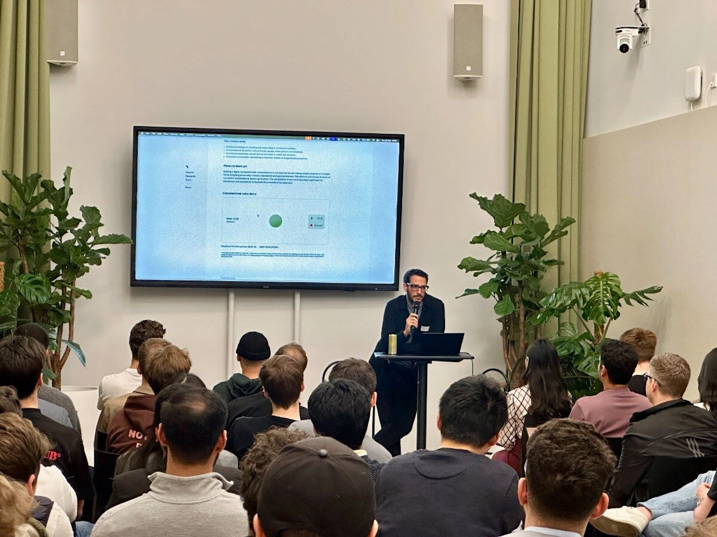(Photo) A man is giving a presentation to an audience in a room. The presentation is displayed on a large screen behind him. Text: Top components * Components: building blocks enabling you to compose reusable interfaces. * Composition: building interfaces by combining components. * State: components can maintain internal state, enabling interactivity. * Props: components can receive data from parent components. * Declarative rendering: React automatically updates the right places when your data changes. Make up from them yet? React lets you compose complex UIs from small and isolated pieces of code called "components". React has a couple of different kinds of components, but we'll start with React components: these are plain Javascript functions. You can think of them as HTML-like elements that you can write yourself. They're similar to Javascript functions, but they work in isolation and return markup. React components are reusable, which means you can use them to build other components. Conventional video demo Stage: RGB RGB: 0, 255, 0 person | indoor | multiple people, presentation screen | candid | Colors: #D3D3D3, #000000, #FFFFFF Note: The image shows a real-life scene with people and objects, indicating it's a photograph rather than an illustration, logo, or banner. There's also a presentation screen, but the overall image is a photo of the event.