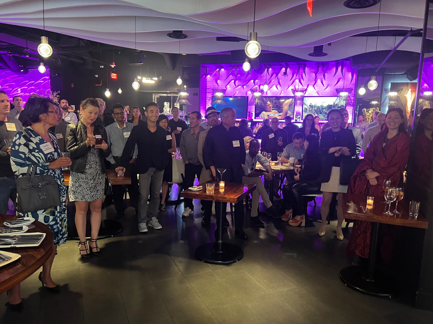 (Photo) A photo of a group of people gathered in a dimly lit bar or restaurant setting. people | indoor | group of people, bar/restaurant setting, dim lighting | candid Note: The image is a real-life captured scene of people in a social setting, indicative of a photograph. It's not a drawing, logo, or banner, and doesn't fit other specific categories.